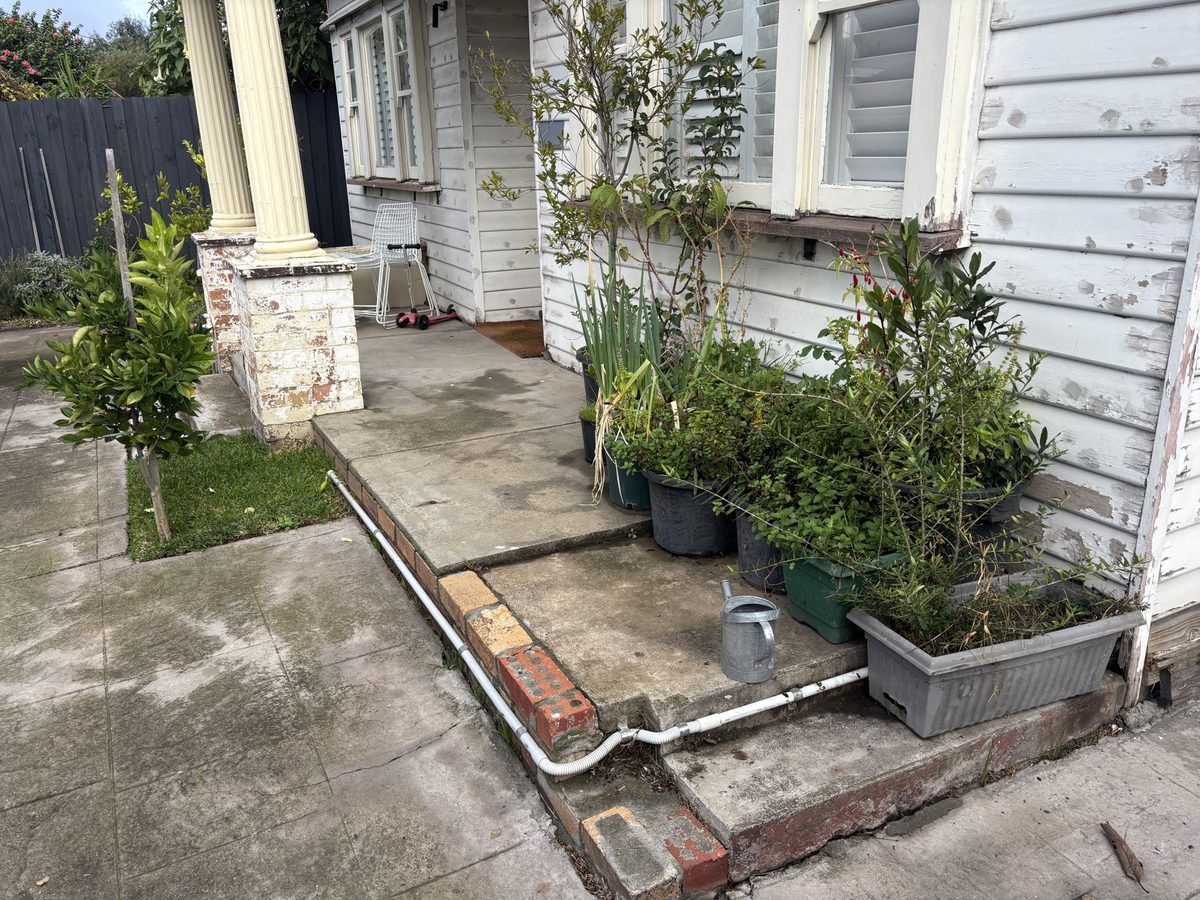 Cracked concrete verandah with weeds and pot plants, before the deck went in