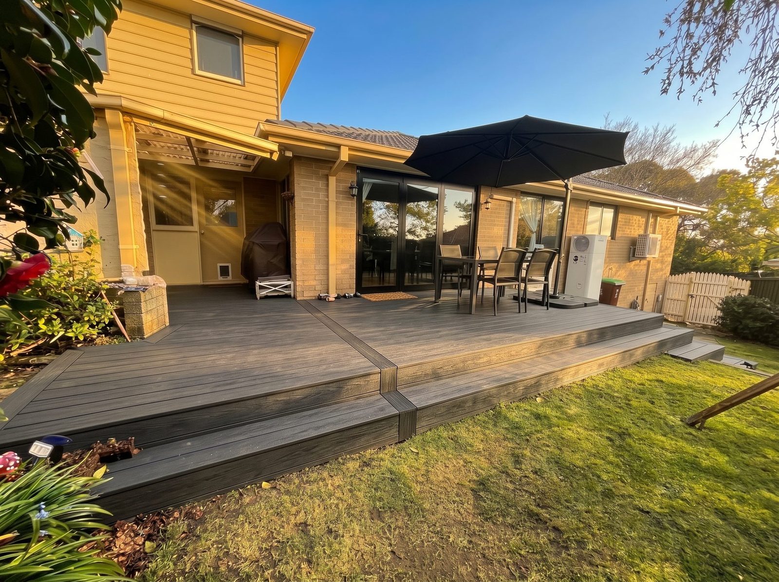 The same grey composite deck photographed in late afternoon sun, showing the full run along the back of the house